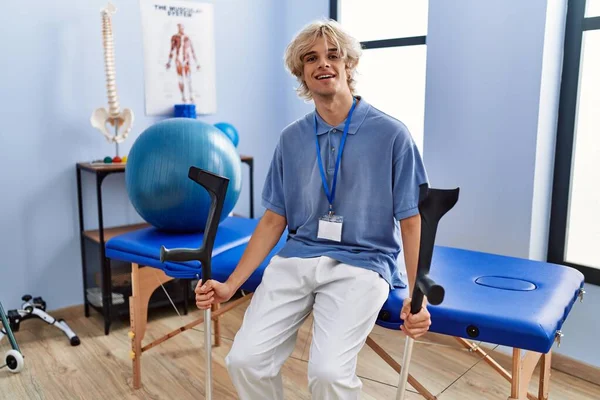 Mladý Blonďatý Muž Pysioterapeut Úsměvem Jistý Držení Berle Rehabilitační Klinice — Stock fotografie
