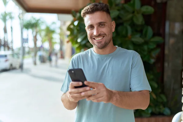 若いヒスパニック男笑顔自信を持って使用してスマートフォンでストリート — ストック写真