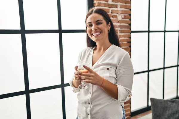 stock image Young beautiful hispanic woman drinking glass of wine standing at home