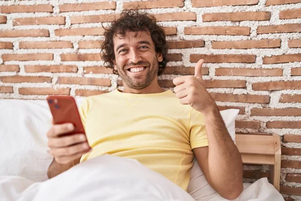 Latynos Młody Człowiek Pomocą Smartfona Łóżku Uśmiechnięty Szczęśliwy Pozytywny Kciuk — Zdjęcie stockowe