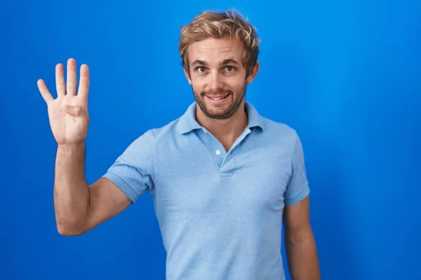 白种人站在蓝色的背景上 用四号手指指指着 面带微笑 自信而快乐 — 图库照片