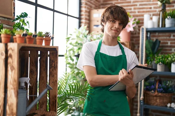 Young blond man florist smiling confident writing on document at flower shop