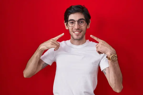 Jonge Spaanse Man Staat Rode Achtergrond Glimlachend Vrolijk Tonen Wijzen — Stockfoto