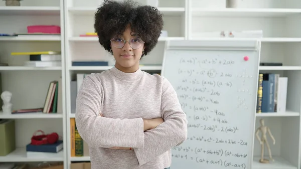 若いアフリカ系アメリカ人の女性教員が大学の教室で腕を組んで立って数学のレッスンを教えています — ストック写真