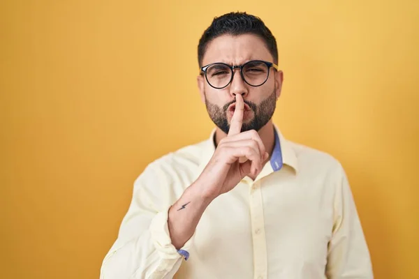 ビジネス用の服を着たヒスパニック系の若者とメガネが唇に指で静かにするように求めています 沈黙と秘密の概念 — ストック写真