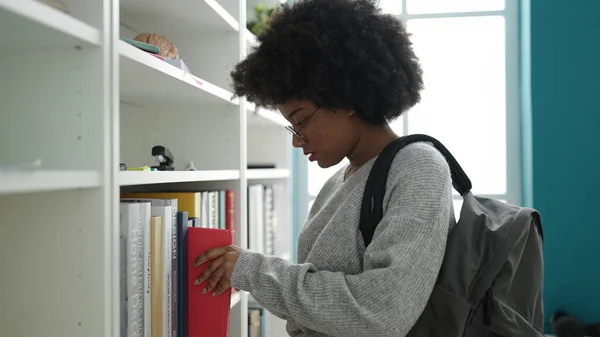 在图书馆大学拿着书架的非洲裔美国女学生 — 图库照片