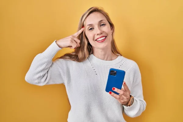 スマートフォンの入力メッセージを使用して若いブロンドの女性は 1本の指で頭を指して笑顔 素晴らしいアイデアや考え 良い記憶 — ストック写真