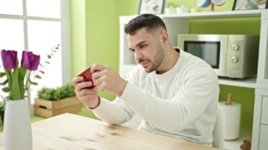 İspanyol asıllı genç bir adam yemek odasında masada oturmuş video oyunu oynuyor.