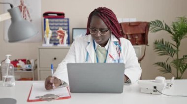 Saçlarını ördüren Afrikalı kadın klinikte laptopunu kullanıyor.