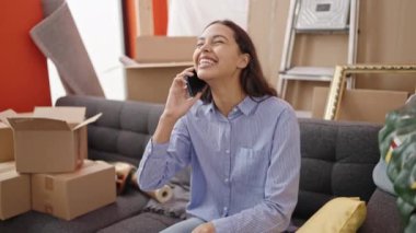 Genç, güzel, İspanyol bir kadın gülümsüyor. Telefonda konuşuyor. Yeni evindeki koltukta oturuyor.