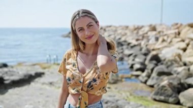 Young blonde woman smiling confident standing at seaside