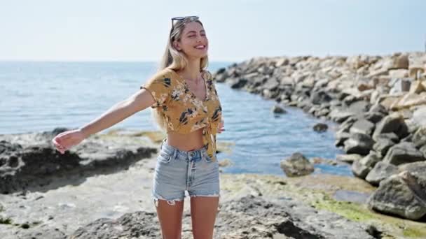 年轻的金发女子带着自信的微笑站在海边 张开双臂 — 图库视频影像