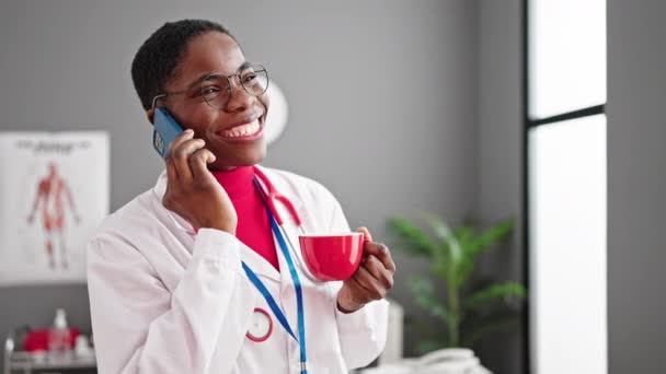 Αφροαμερικανή Γιατρός Πίνοντας Καφέ Μιλώντας Στο Smartphone Στην Κλινική — Αρχείο Βίντεο