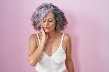 Middle age woman with grey hair standing over pink background touching mouth with hand with painful expression because of toothache or dental illness on teeth. dentist 