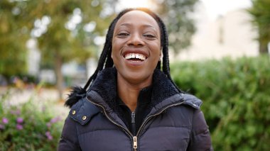 Afro-Amerikalı kadın parkta kendinden emin bir şekilde gülümsüyor.