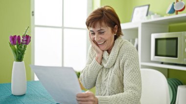 Olgun İspanyol kadın yemek odasındaki masada oturmuş evrak okuyor.