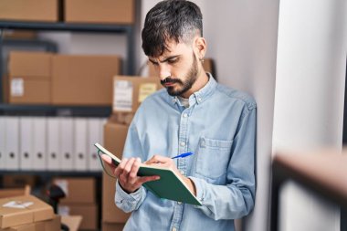 Young hispanic man ecommerce business worker writing on notebook at office