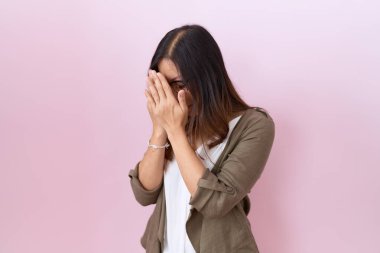 Orta yaşlı Çinli kadın pembe arka planda gözlük takıyor ve ağlarken suratını ellerle kapatıyor. depresyon kavramı. 