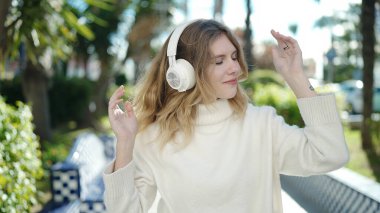 Young blonde woman listening to music and dancing at park