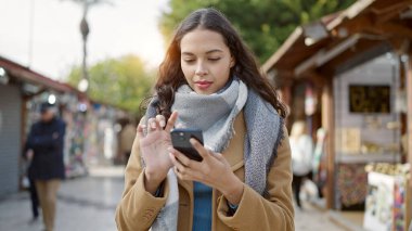 Piyasada gülümseyen akıllı telefon kullanan genç, güzel İspanyol kadın.