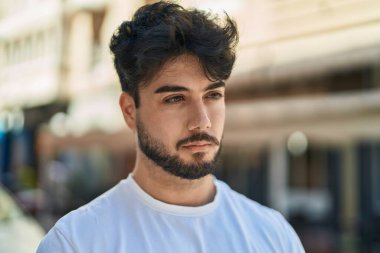 Young hispanic man with relaxed expression standing at street