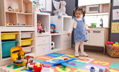 Adorable hispanic girl standing with relaxed expression at kindergarten