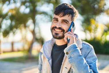 Genç İspanyol adam gülümsüyor. Parktaki akıllı telefondan konuşuyor.