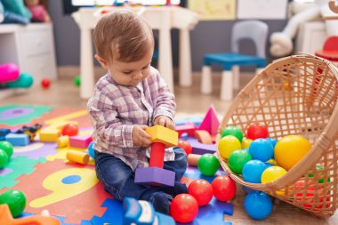 Anaokulunda yerde taşaklarıyla oynayan sevimli beyaz çocuk.