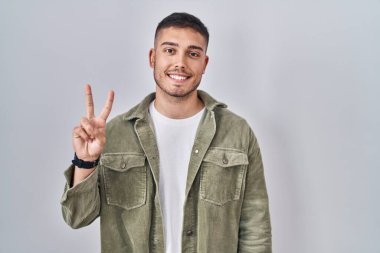 İzole edilmiş arka planda duran genç İspanyol adam iki numarayı gösterip işaret ederken kendinden emin ve mutlu bir şekilde gülümsüyor.. 