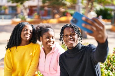 African american friends making selfie by the smartphone sitting on bench at park