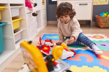 Anaokulunda yerde oturmuş süpermarket oyunu oynayan sevimli İspanyol çocuk.