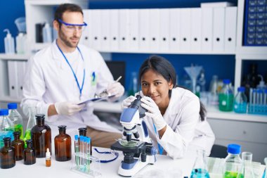 Man and woman scientists using microscope working at laboratory