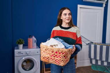Çamaşır odasında çamaşır sepetini tutan kendine güvenen genç bir kadın.