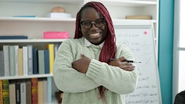 Saçları örgülü Afrikalı kadın üniversite kütüphanesinde gülümseyen beyaz yönetim kurulunun yanında duruyor.