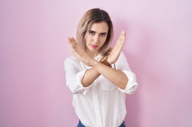 Pembe arka planda duran güzel bir kadın. Reddedilmiş yüz ifadesi. Kollarını kavuşturup negatif işaret veriyor. 