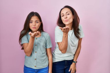 Genç anne ve kızı pembe arka planda dikilip kameraya bakıyorlar. Canlı yayında öpüşüyorlar ve güzel ve seksiler. aşk ifadesi. 