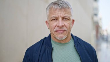 Middle age grey-haired man standing with serious expression at street