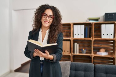 Genç, güzel İspanyol iş kadını. Ofiste kendinden emin bir şekilde kitap okurken gülümsüyor.