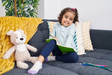 Evdeki kanepede oturan sevimli İspanyol kız deftere yazı yazıyor.