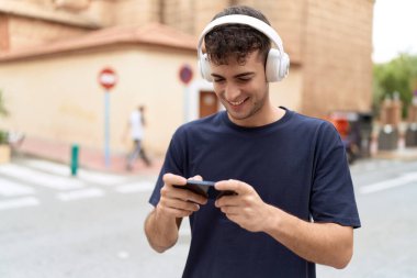 Young hispanic man smiling confident playing video game at street