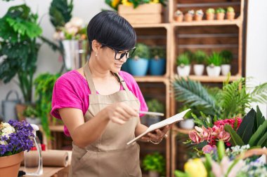 Middle age chinese woman florist smiling confident reading notebook at flower shop