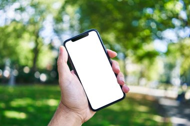Akıllı telefonu tutan adam parkta beyaz ekranı gösteriyor.