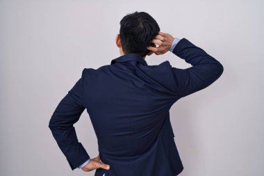 Genç Asyalı takım elbiseli ve kravatlı bir adam elleri kafasında şüpheyi geriye doğru düşünüyor. 