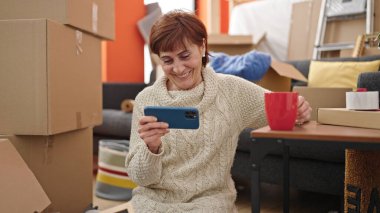 Olgun İspanyol kadın akıllı telefon kullanıyor. Yeni evinde şarap içiyor.