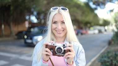 Young blonde woman tourist using vintage camera at street