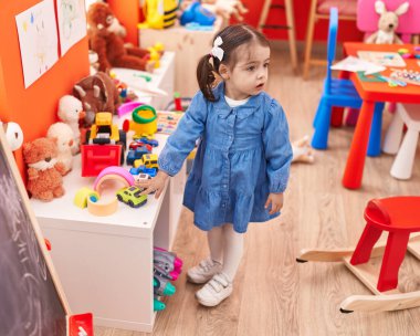 Adorable hispanic girl standing with relaxed expression at kindergarten