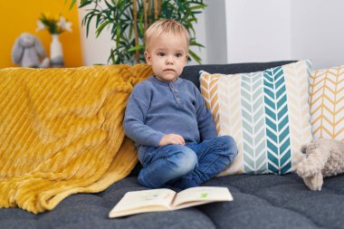 Evinde rahat bir ifadeyle kanepede oturan sevimli beyaz çocuk.