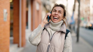 Orta yaşlı İspanyol kadın gülümsüyor. Akıllı telefondan konuşuyor.