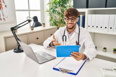 Young arab man wearing doctor uniform having video call at clinic