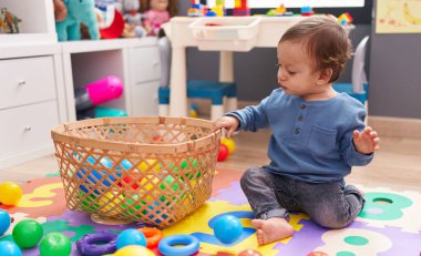 Anaokulunda yerde oturmuş toplarla oynayan sevimli İspanyol çocuk.